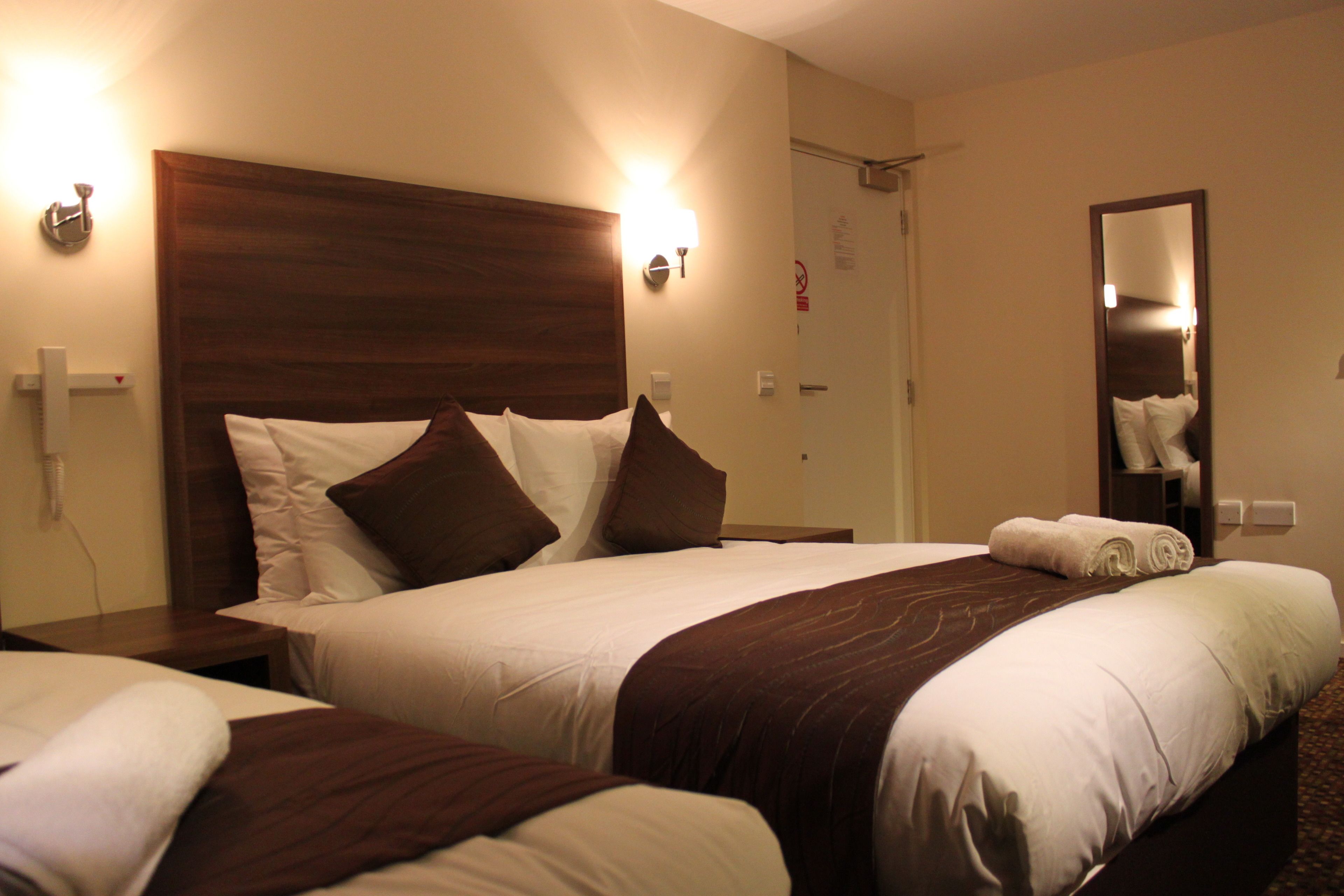 Une chambre d’hôtel avec deux lits, une tête de lit en bois, une table de chevet, un miroir et une porte de salle de bain.