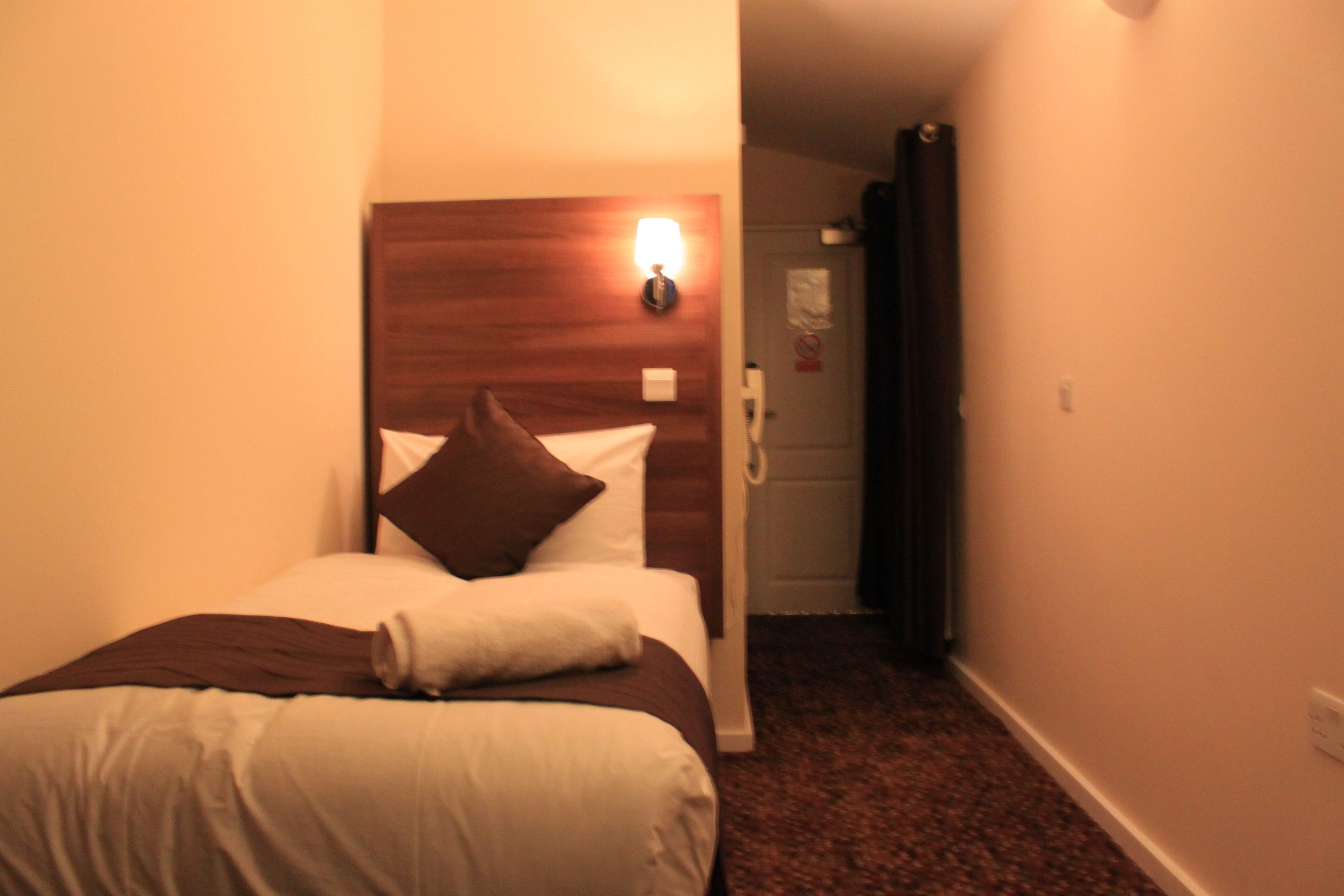 Une chambre d’hôtel avec un lit, une tête de lit en bois, une table de chevet, une lampe et une porte donnant sur une autre pièce.