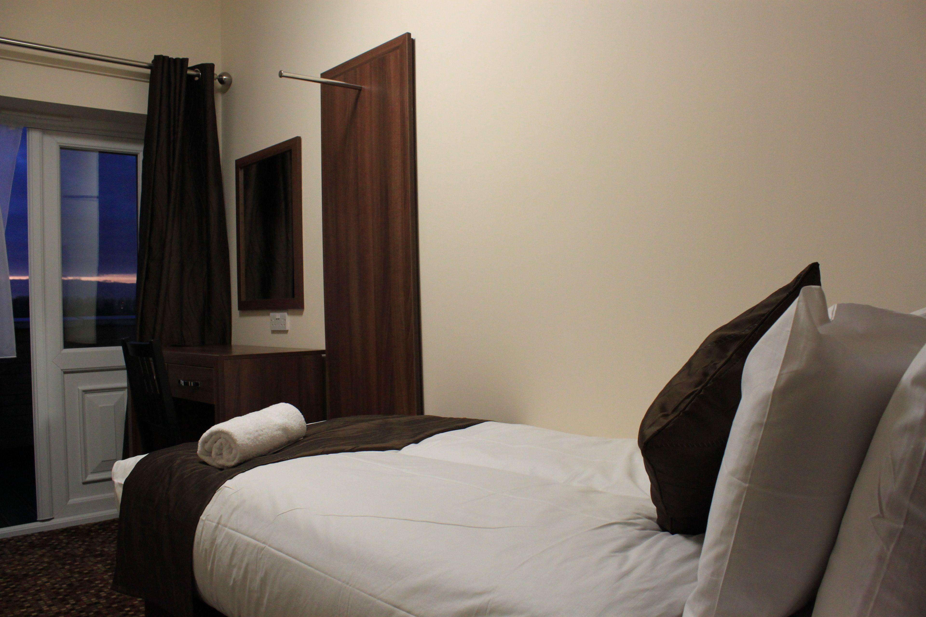 Una habitación de hotel con cama, escritorio de madera, espejo y ventana con cortinas.