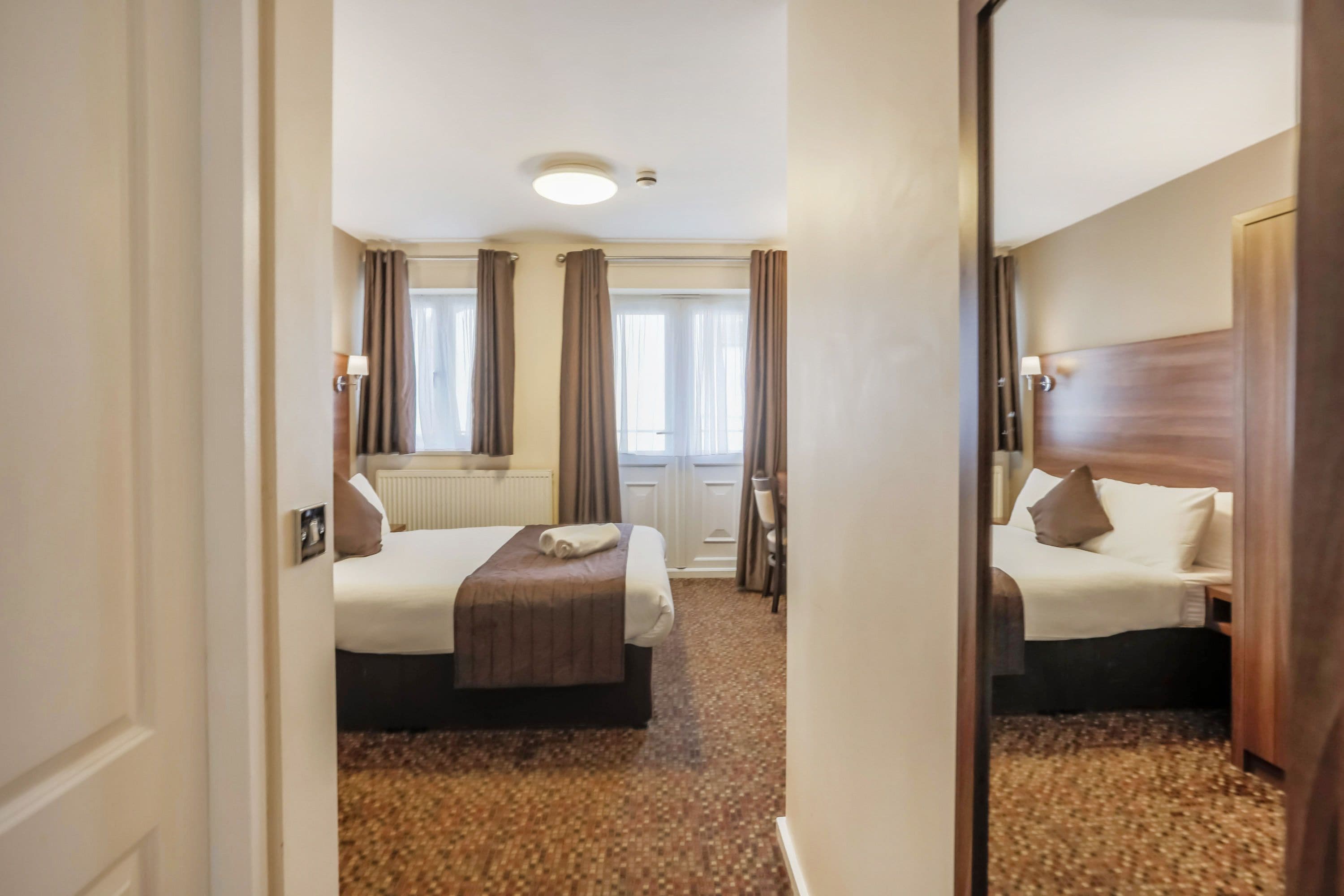 A hotel room with a bed, a chair, a window with curtains, and a radiator.