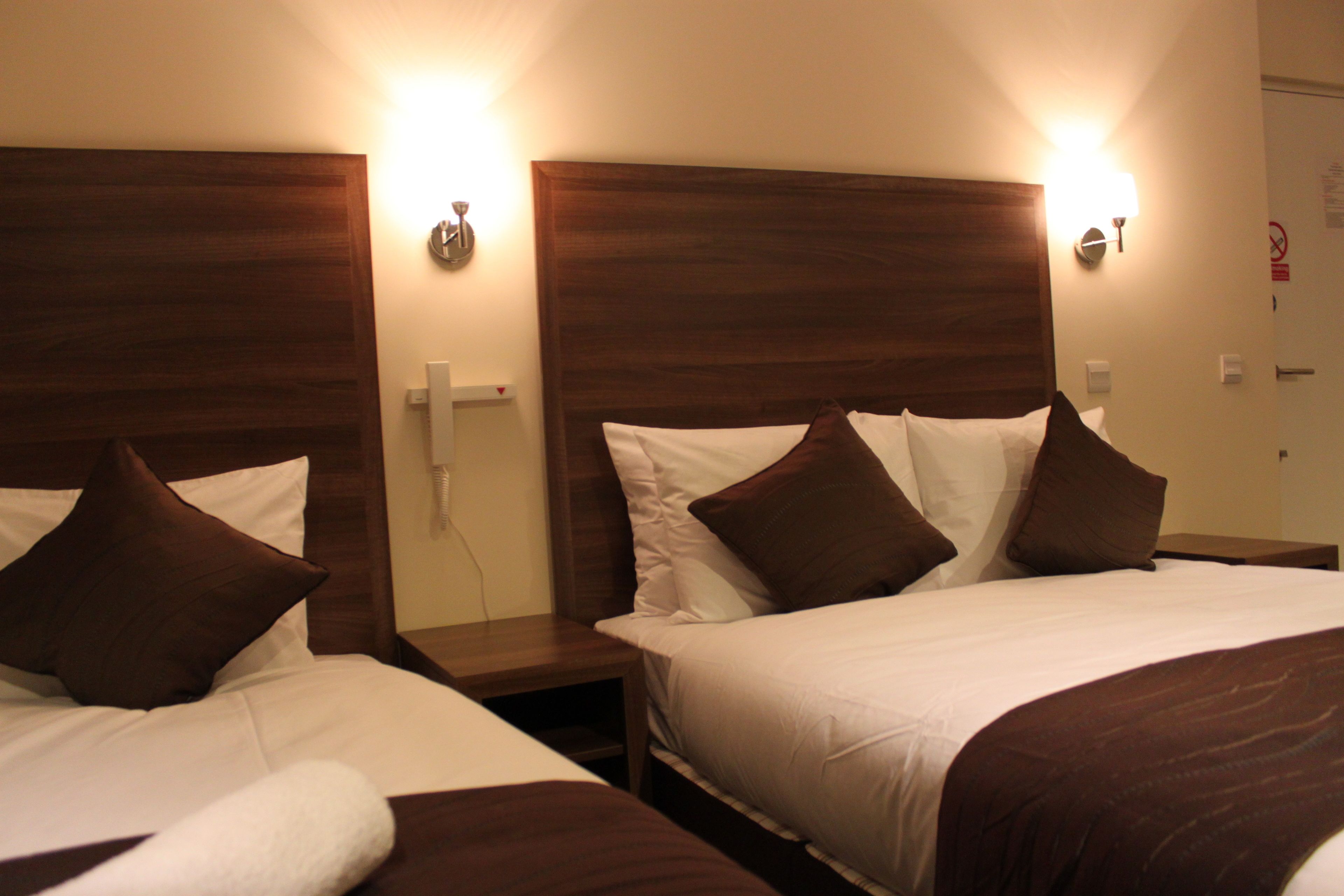 Two adjacent hotel rooms with wooden headboards, white bedding, and brown throw pillows.