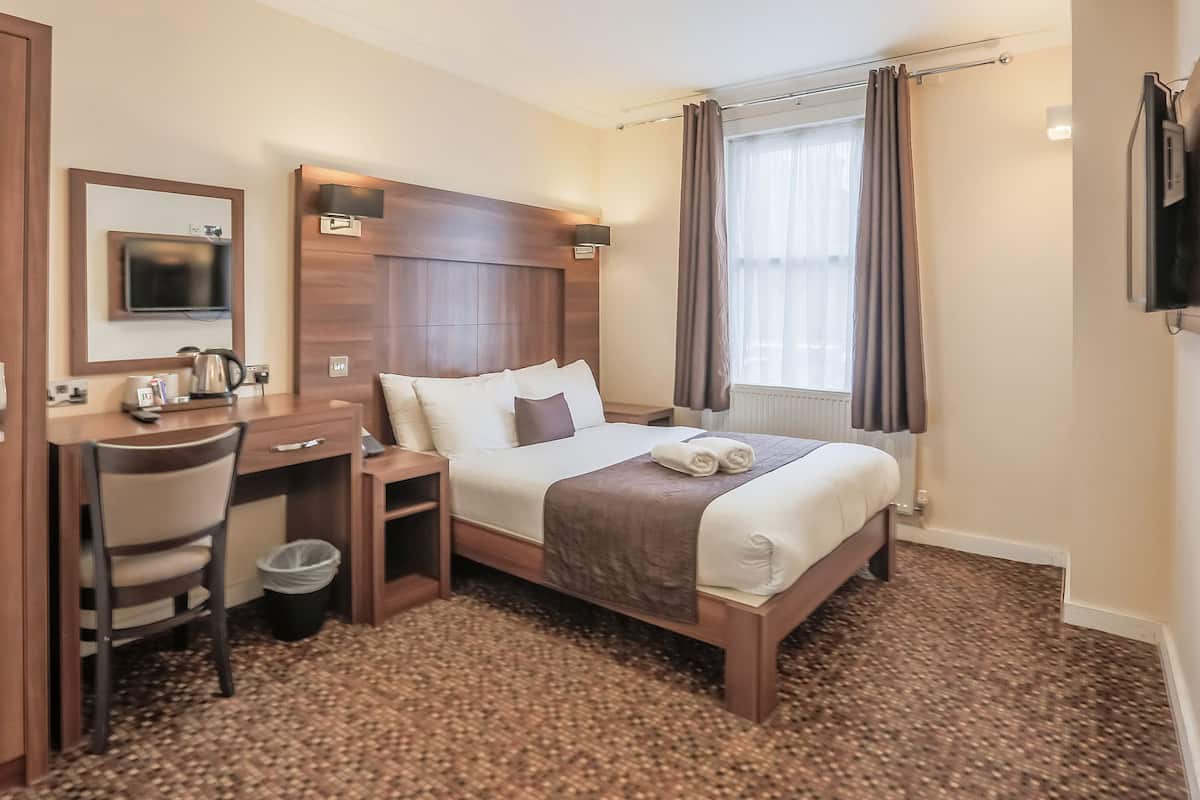 Ett hotellrum med en säng, ett skrivbord, en stol, en tv och ett fönster med gardiner.