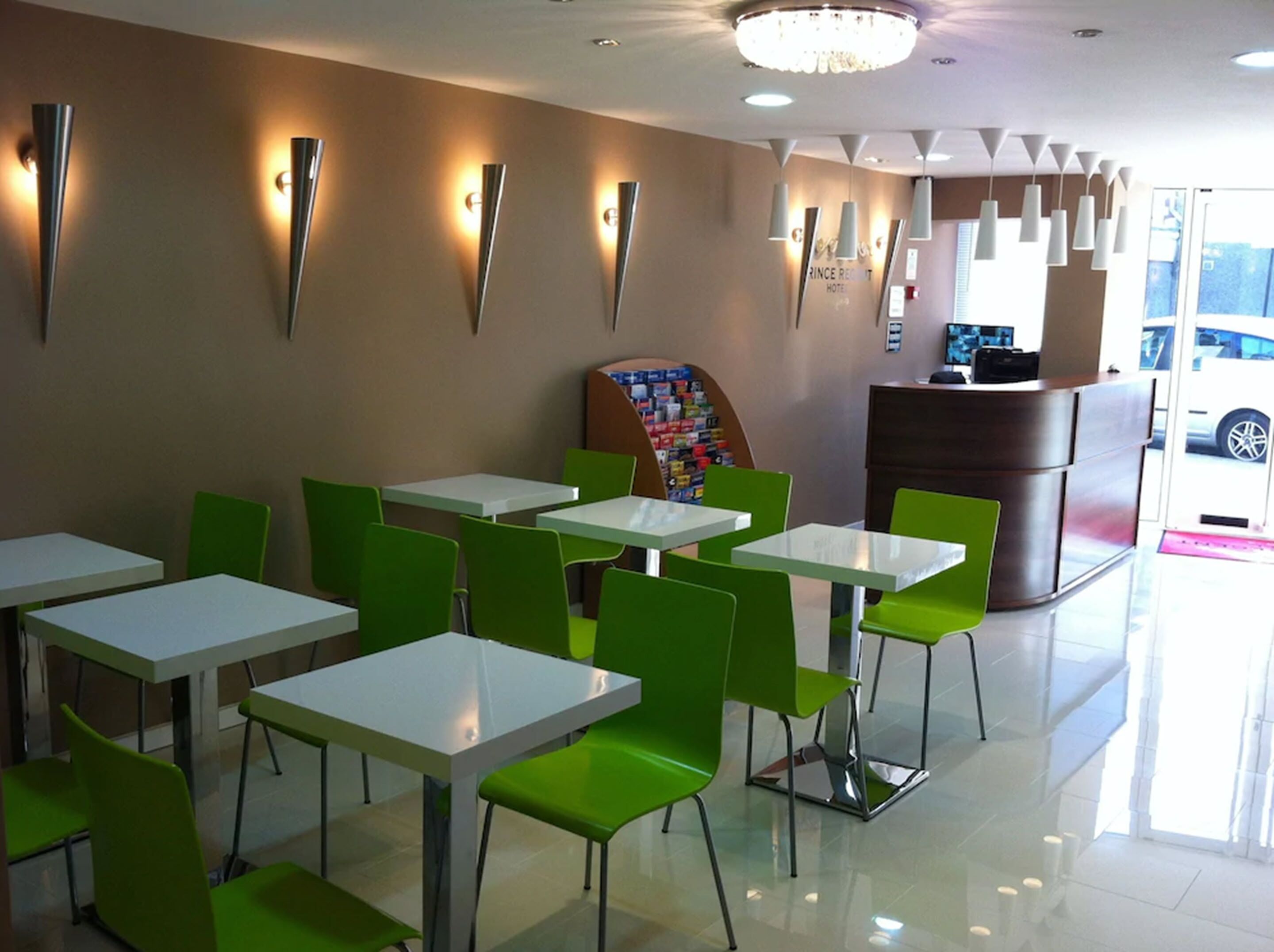 A hotel lobby with green chairs and white tables, a reception desk, and a chandelier.