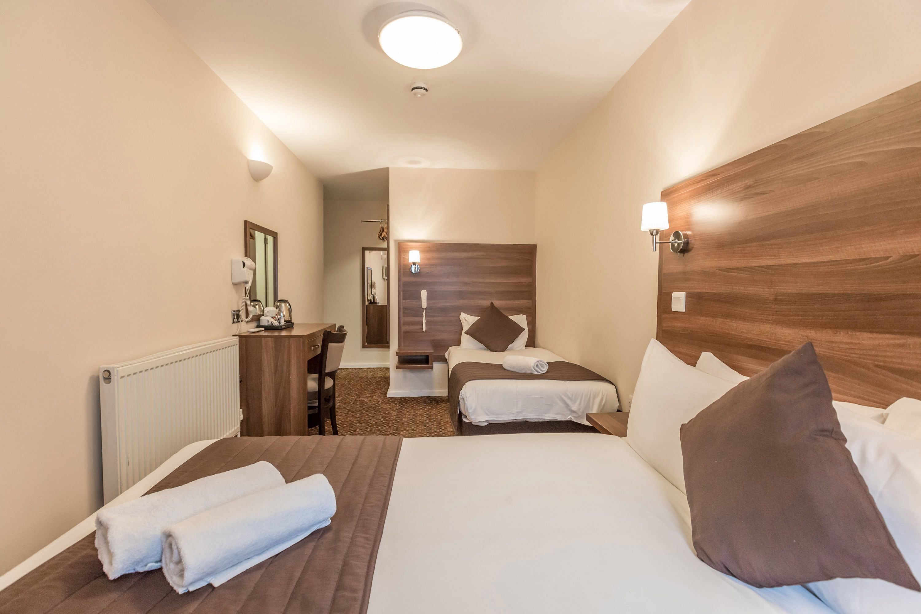 A hotel room with two beds, a desk, and a mirror.