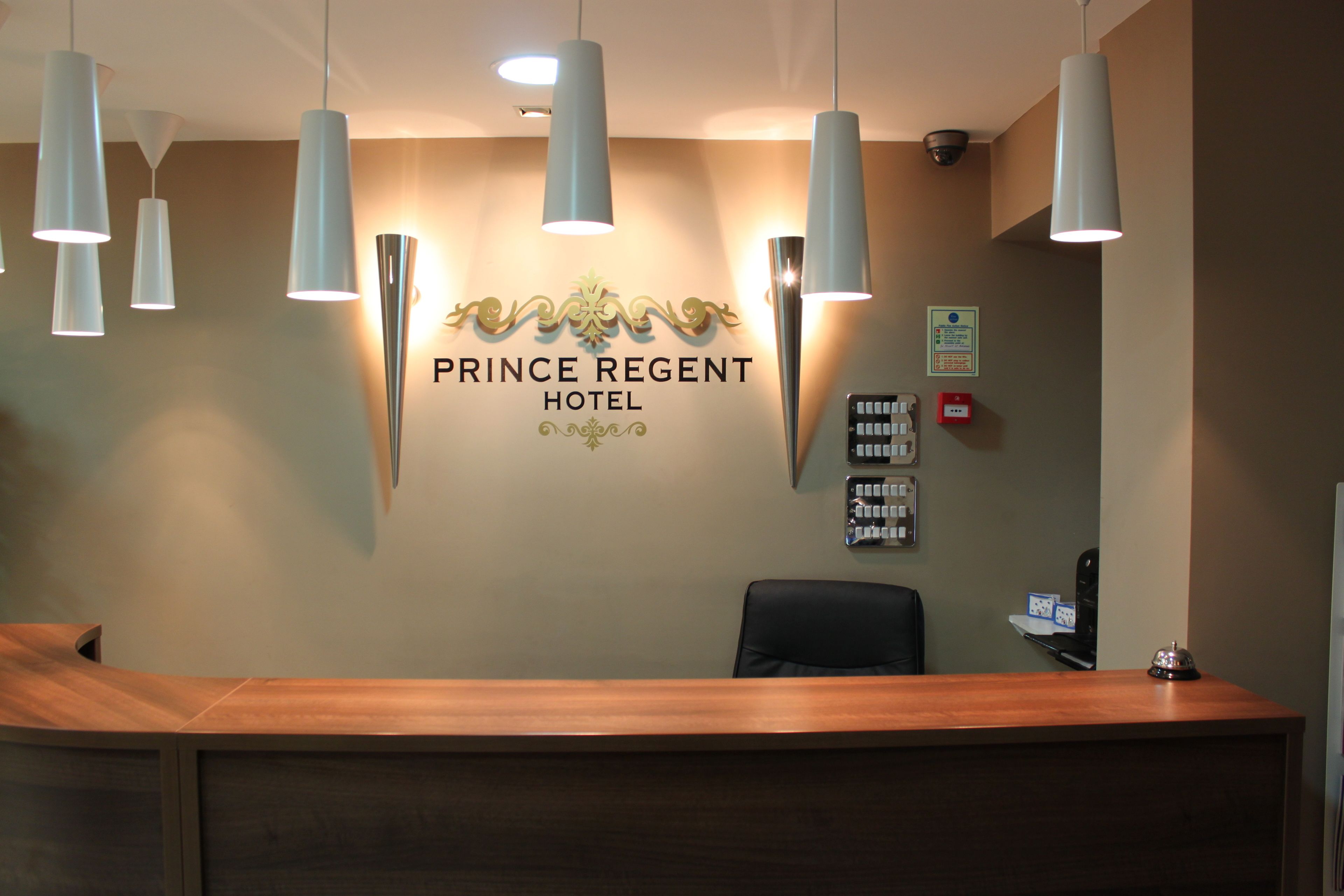 Mostrador de recepción de hotel con un cartel que dice "PRINCE REGENT HOTEL" y una silla negra al frente.