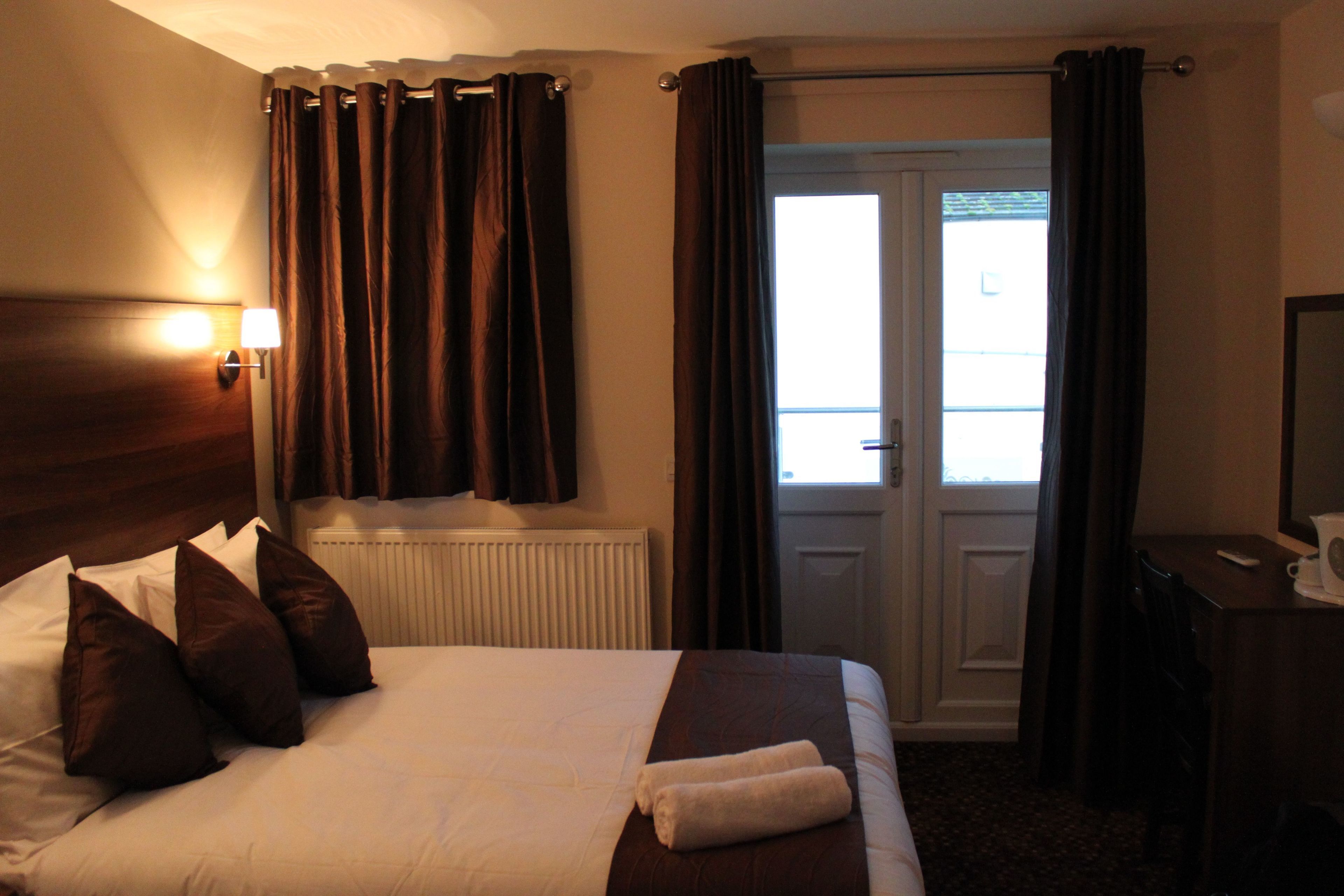 A hotel room with a bed, a desk, a lamp, and a view of the outside.