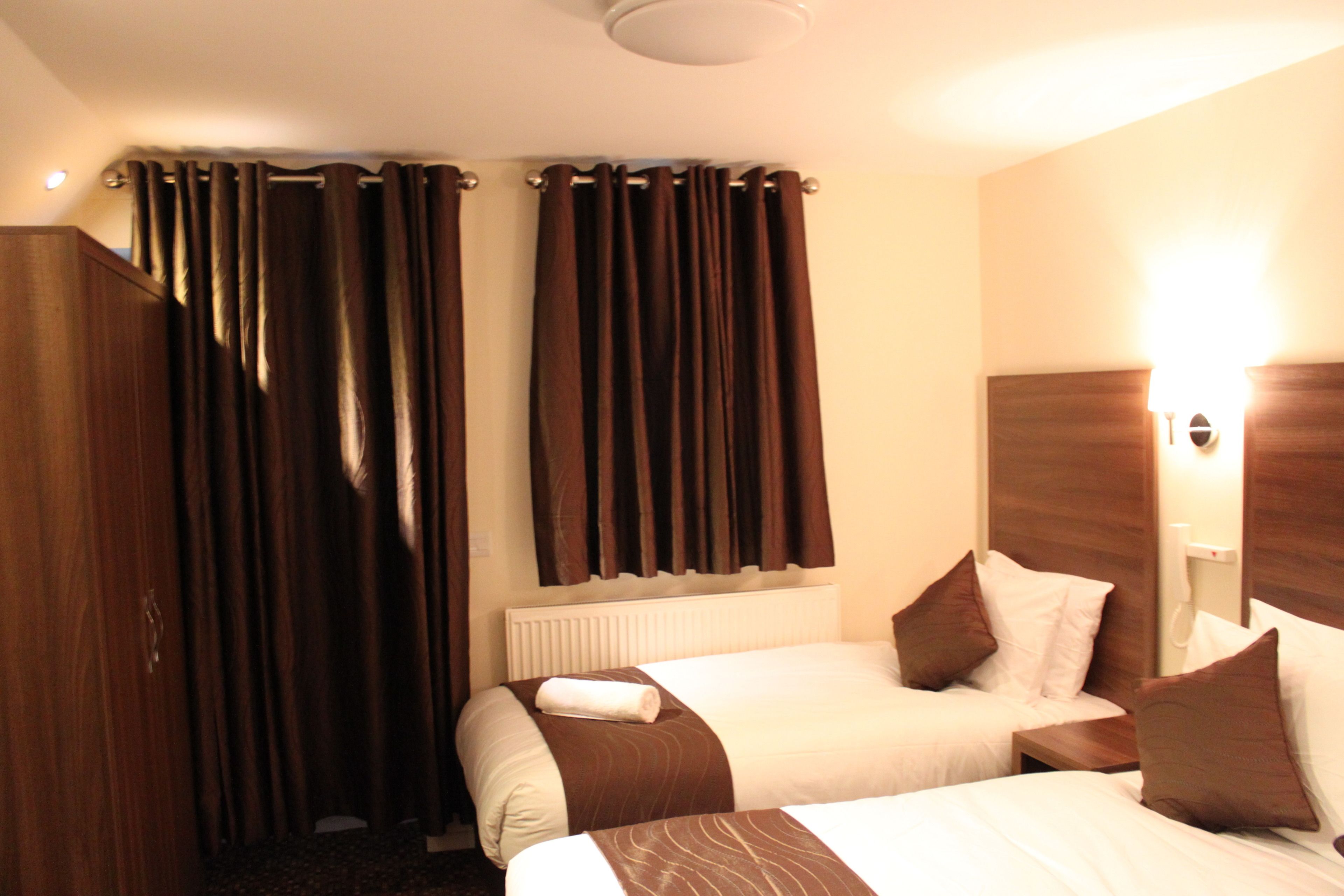Habitació d'hotel amb dos llits, un armari de fusta i una finestra amb cortines.