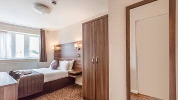 A hotel room with a bed, bedside table, lamp, wardrobe, and a window with curtains.