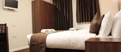 A hotel room with a bed, a TV mounted on the wall, a wardrobe, and a desk.