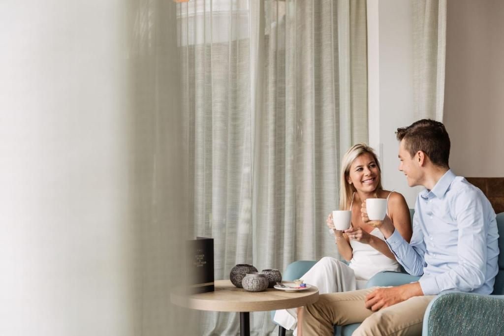 Una pareja sentada en un sofá con una mesa entre ambos, sosteniendo tazas.