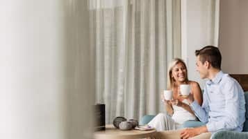 A couple sitting on a sofa with a table between them, holding cups.