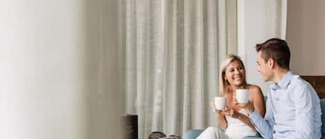 Una pareja sentada en un sofá con una mesa entre ambos, sosteniendo tazas.