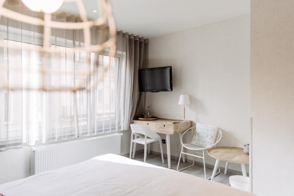 Habitación de hotel con cama, un escritorio y una silla, un televisor montado en la pared y una ventana con cortinas.