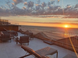 Terraza en la azotea con mobiliario exterior y vistas a la puesta de sol sobre el océano.