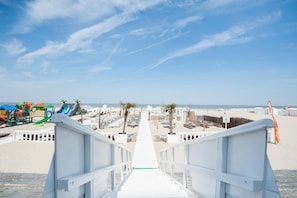 A beachside walkway leading to a sandy beach with a playground and palm trees. - Beach Hotel Helios by CW Hotel Collection (Blankenberge)