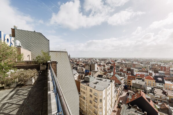 Un edificio de gran altura con techo inclinado y vistas a una zona urbana densamente poblada con diversos edificios.