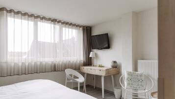 Una habitación de hotel con cama, escritorio, silla, televisor y ventana con cortinas.