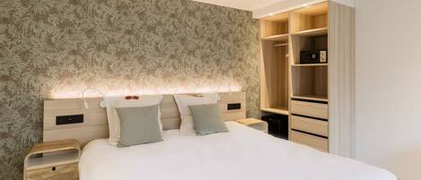Un dormitorio con cama, mesitas de noche, armario y cabecera con iluminación integrada.
