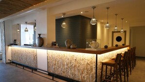 A modern bar area with a stone-textured counter, hanging pendant lights, and wooden bar stools. - Beach Hotel Helios by CW Hotel Collection (Blankenberge)