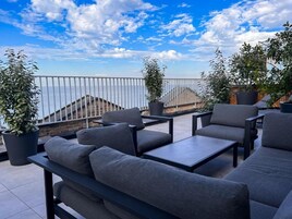 Una terraza en la azotea con asientos al aire libre, plantas en macetas y vistas al mar.