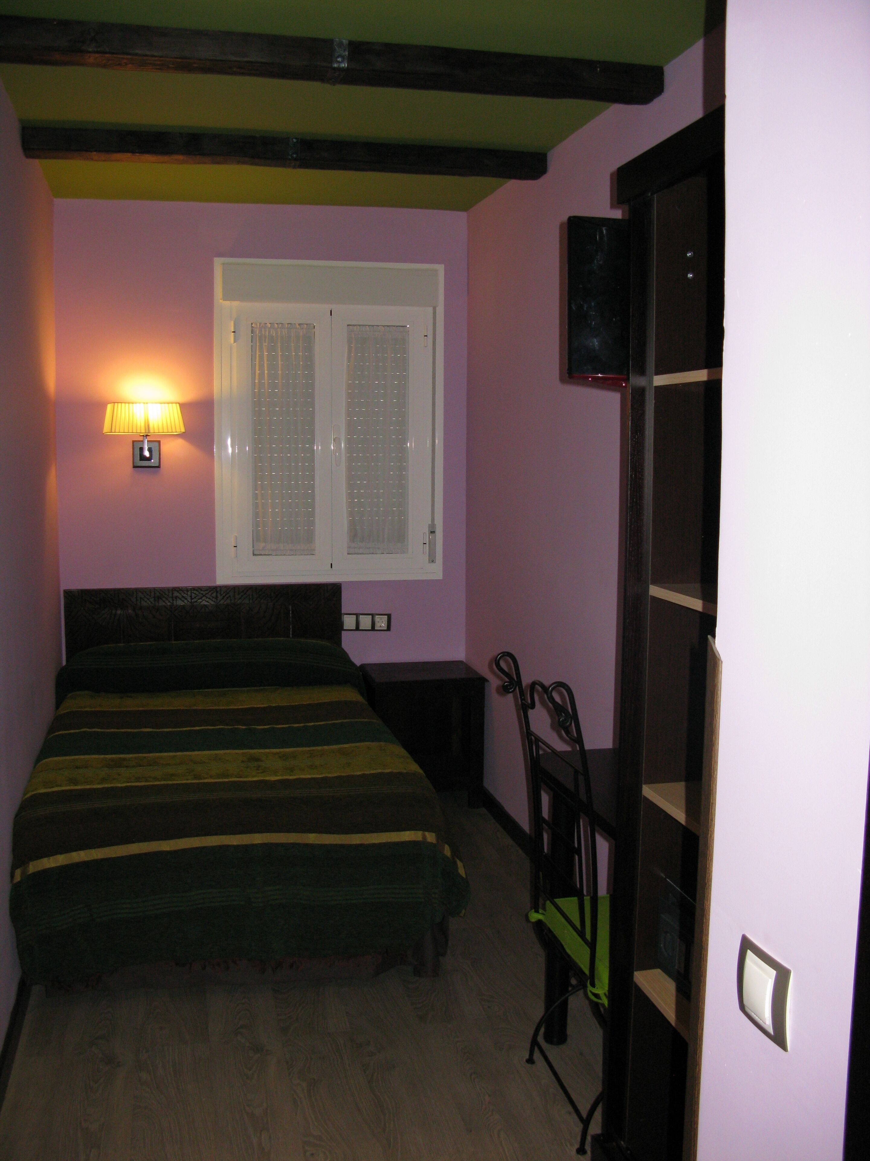 A bedroom with a bed, a nightstand, a lamp, a window, and a door.