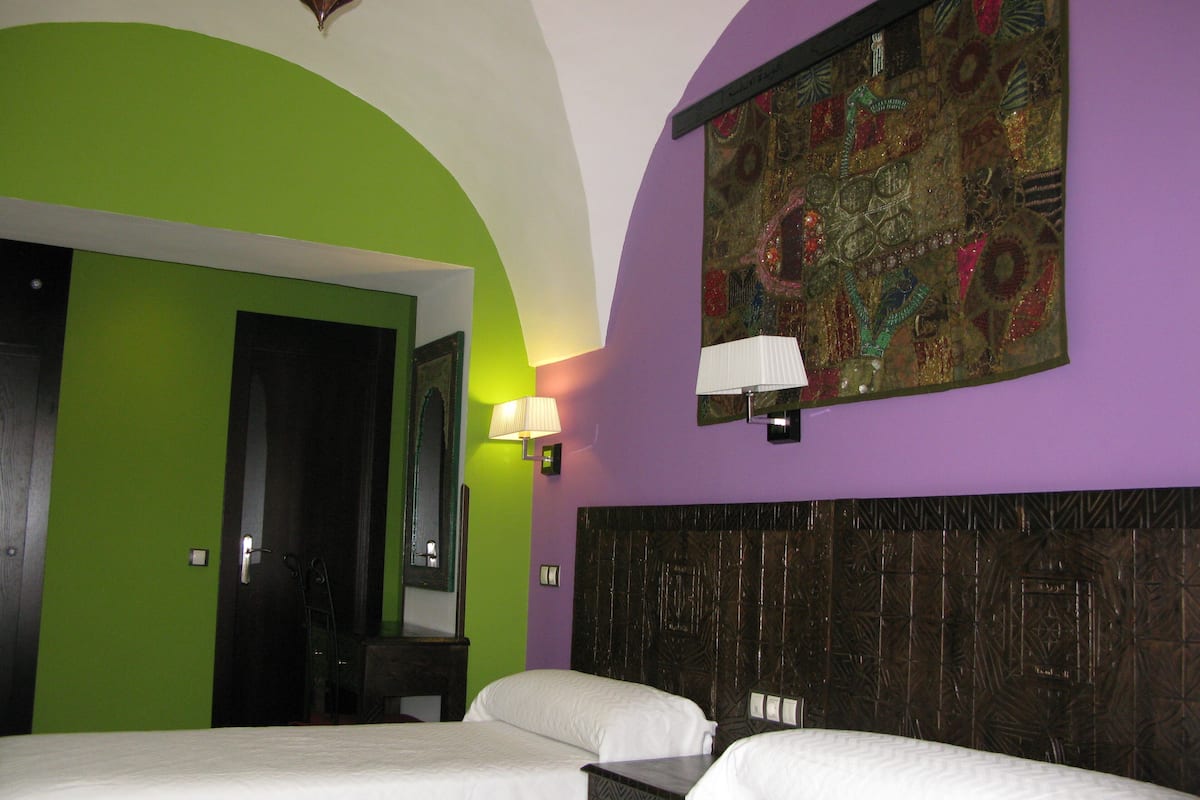 A hotel room with two beds, a green wall, a purple accent wall, and a decorative tapestry.