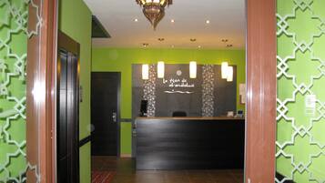 A reception area with a modern design, featuring a reception desk, a patterned wall, and a decorative hanging light fixture.