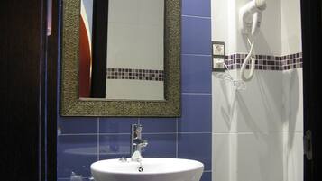 A bathroom with a white sink, a mirror with a decorative frame, a hairdryer, and a towel rack.