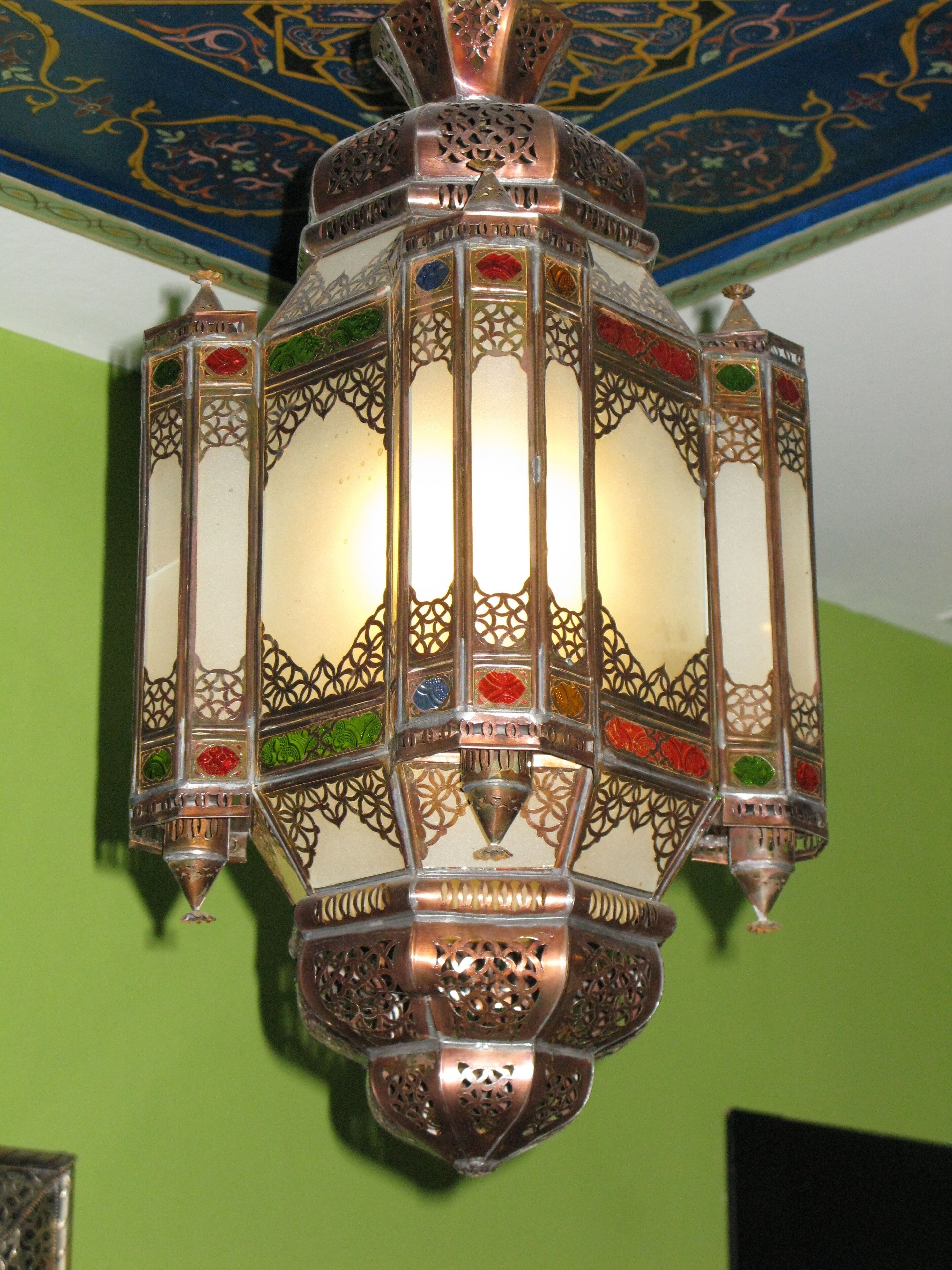 A detailed, ornate wall-mounted light fixture with intricate metalwork and colored glass panels.