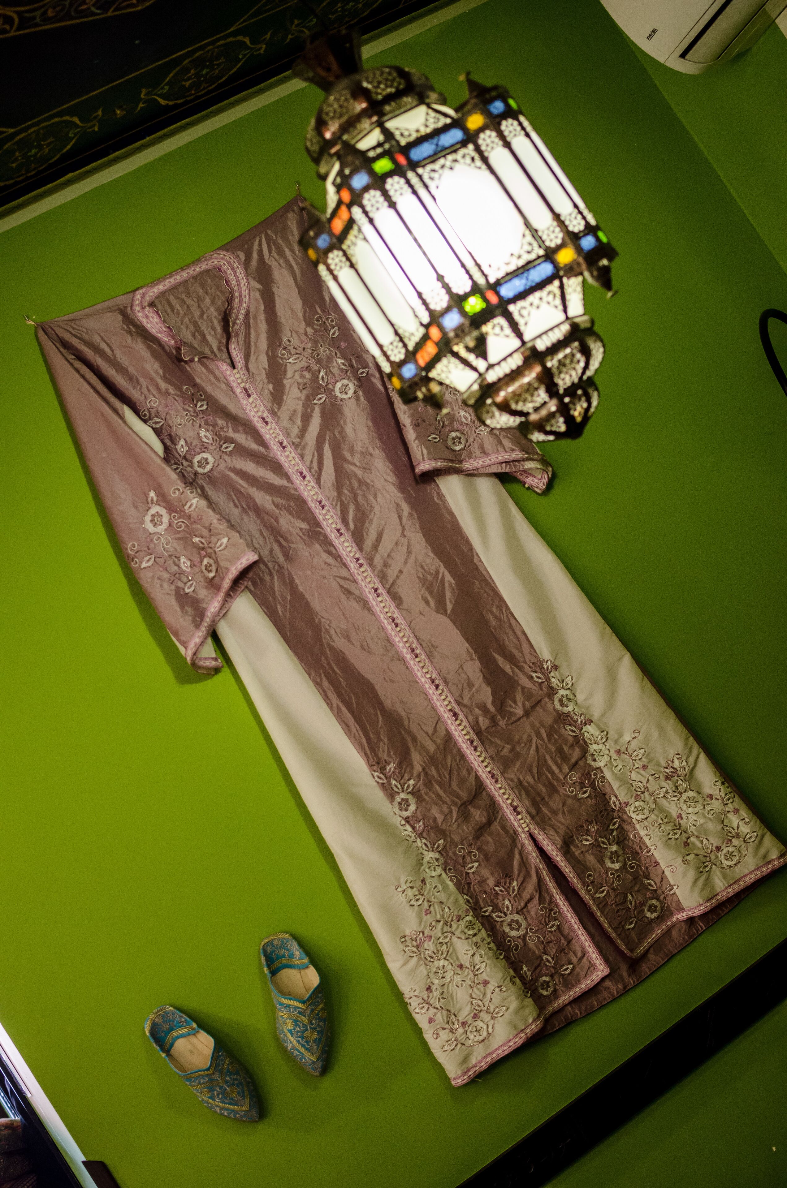 A pool table with a green felt surface, a table lamp, a table tennis paddle, and a pair of table tennis shoes.