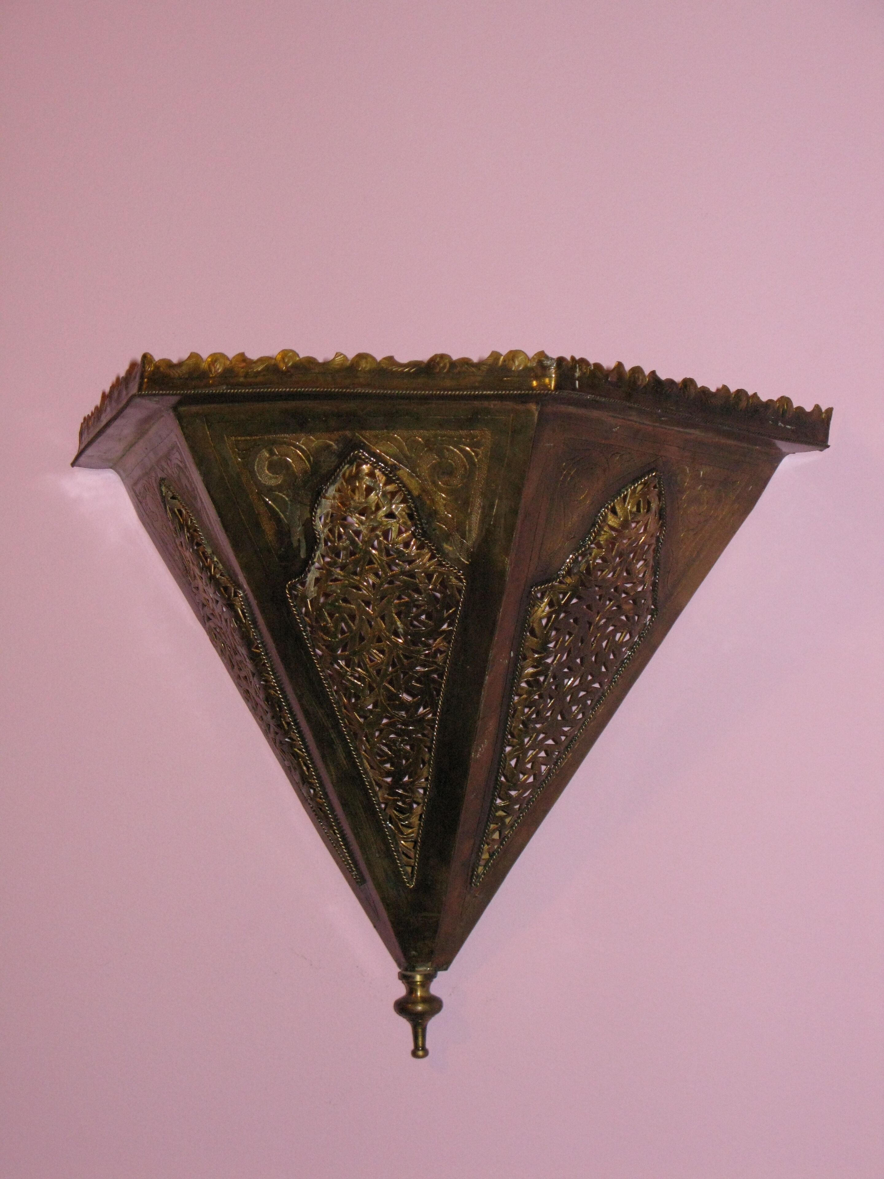A wall-mounted, ornate, triangular-shaped light fixture with intricate patterns and a decorative top edge.