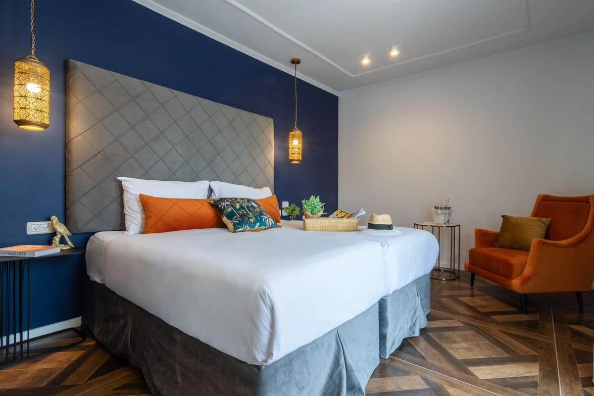 A modern bedroom with a large bed, two hanging lamps, a small side table, and an orange armchair.
