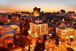 A cityscape at dusk with illuminated buildings, a prominent dome structure, and a central building with a balcony. - The Eldan Hotel (Jerusalem)