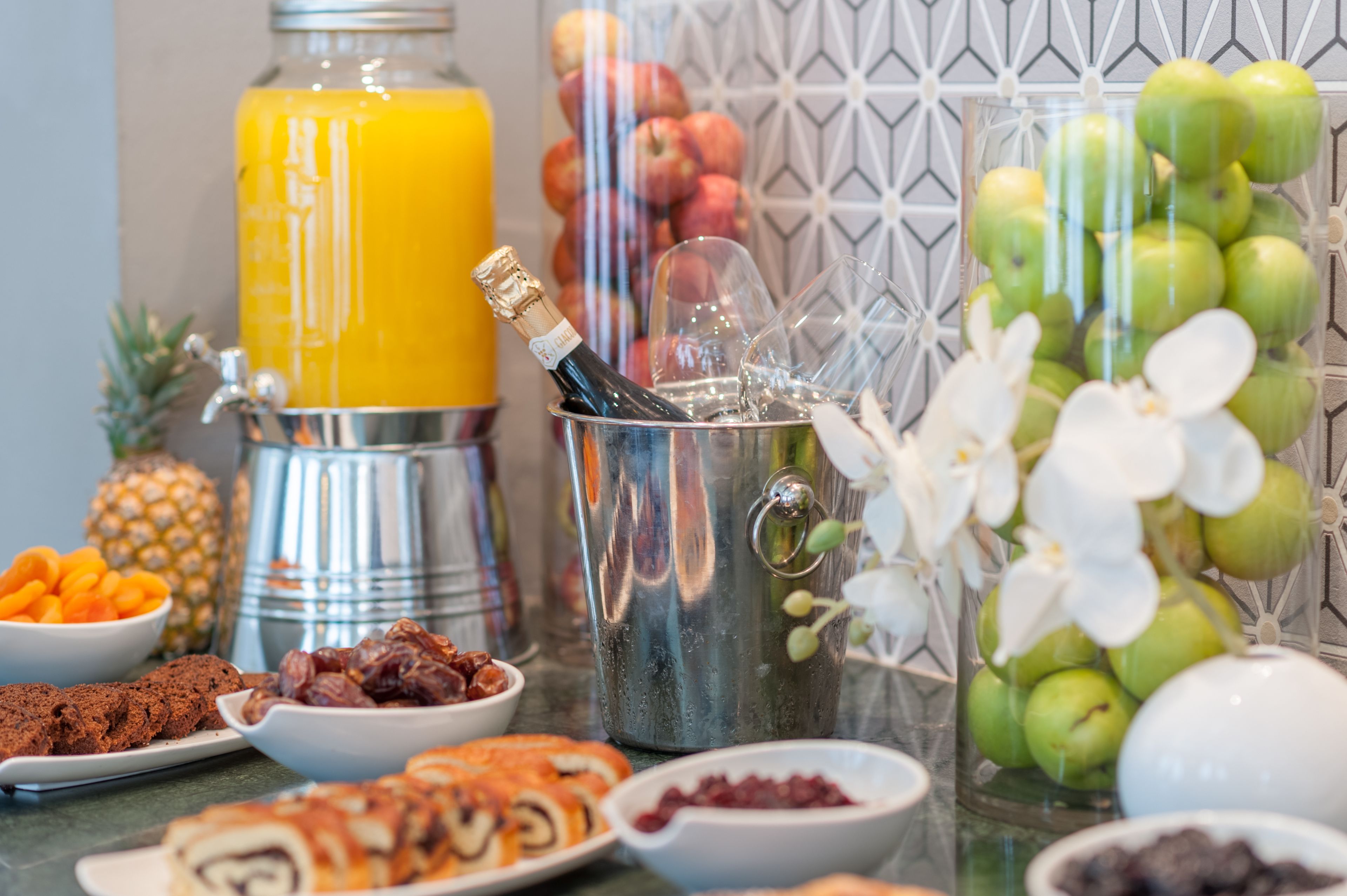 Un ricco buffet per la colazione con diversi cibi, una ciotola di frutta, una bottiglia di champagne e una decorazione a parete.