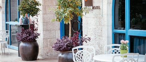 A hotel entrance with a stone facade, large potted plants, and white outdoor furniture.