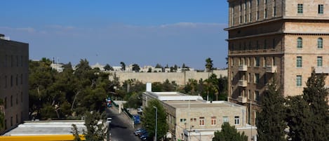 A street lined with parked cars and buildings, including a prominent multi-story structure with balconies.