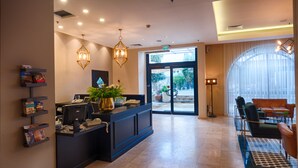 A reception area with a desk, computer, and potted plants. There is a seating area with a sofa and chairs. - The Eldan Hotel (Jerusalem)