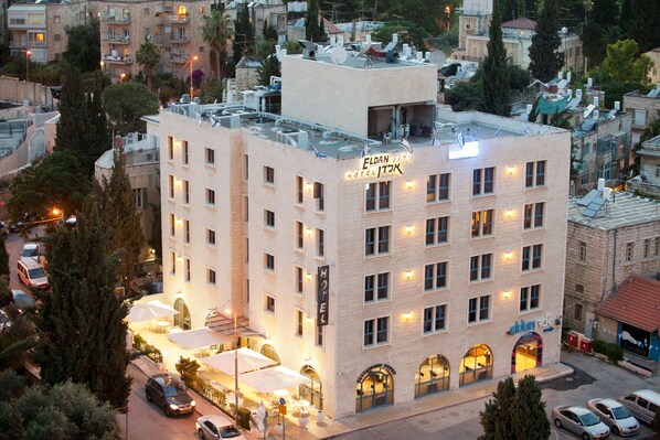 Un hotel de varios pisos con terraza en la azotea, múltiples balcones y una entrada bien iluminada.
