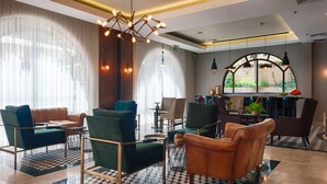 A modern hotel lobby with a checkered floor, green and brown leather sofas, a chandelier, and a view through a large window. - The Eldan Hotel (Jerusalem)