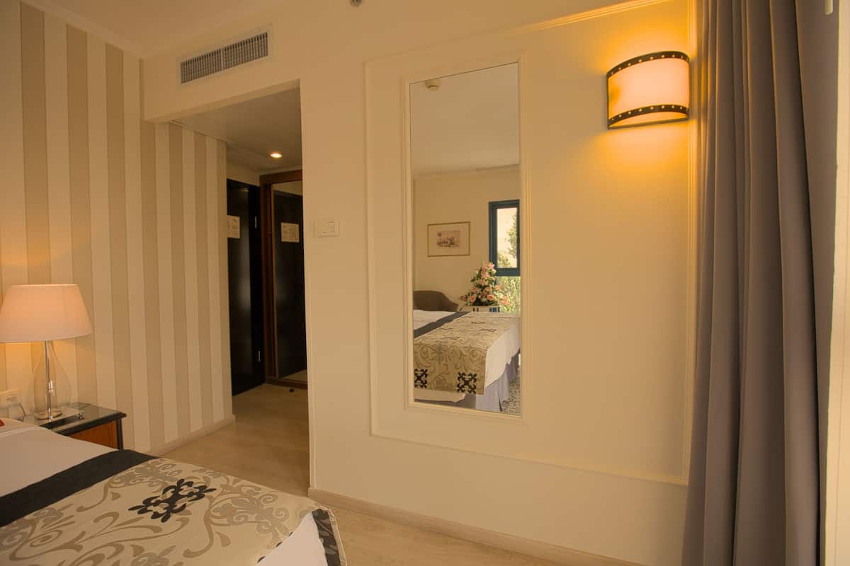 A hotel room with a bed, a nightstand, a lamp, a mirror, and a wall-mounted light fixture.