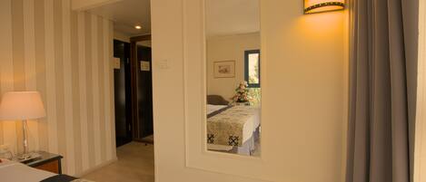 A hotel room with a bed, a nightstand, a lamp, a mirror, and a wall-mounted light fixture.