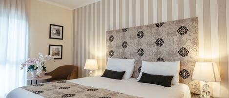 Una habitación de hotel con una cama grande, dos mesitas de noche, una silla y un cabecero decorativo.
