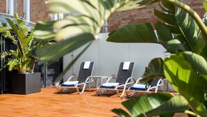 Terraza de madera con sillones de descanso y una planta en maceta.