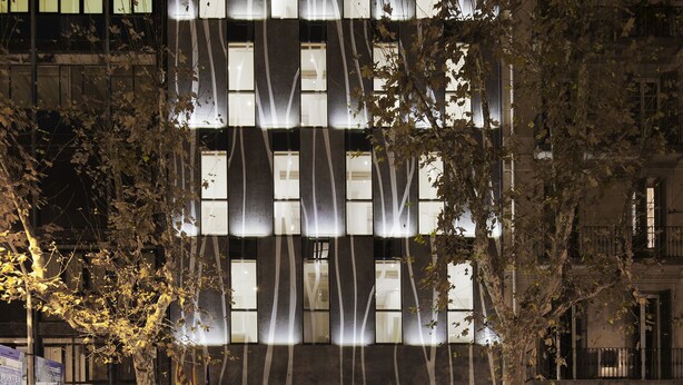 Un edificio moderno con una fachada única que presenta patrones geométricos y ventanas iluminadas.