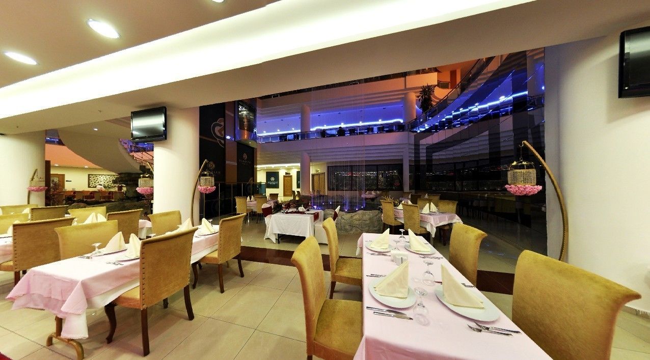 A restaurant with multiple dining tables set with pink tablecloths and gold chairs.