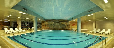 An indoor swimming pool with clear water, surrounded by lounge chairs and a stone wall.