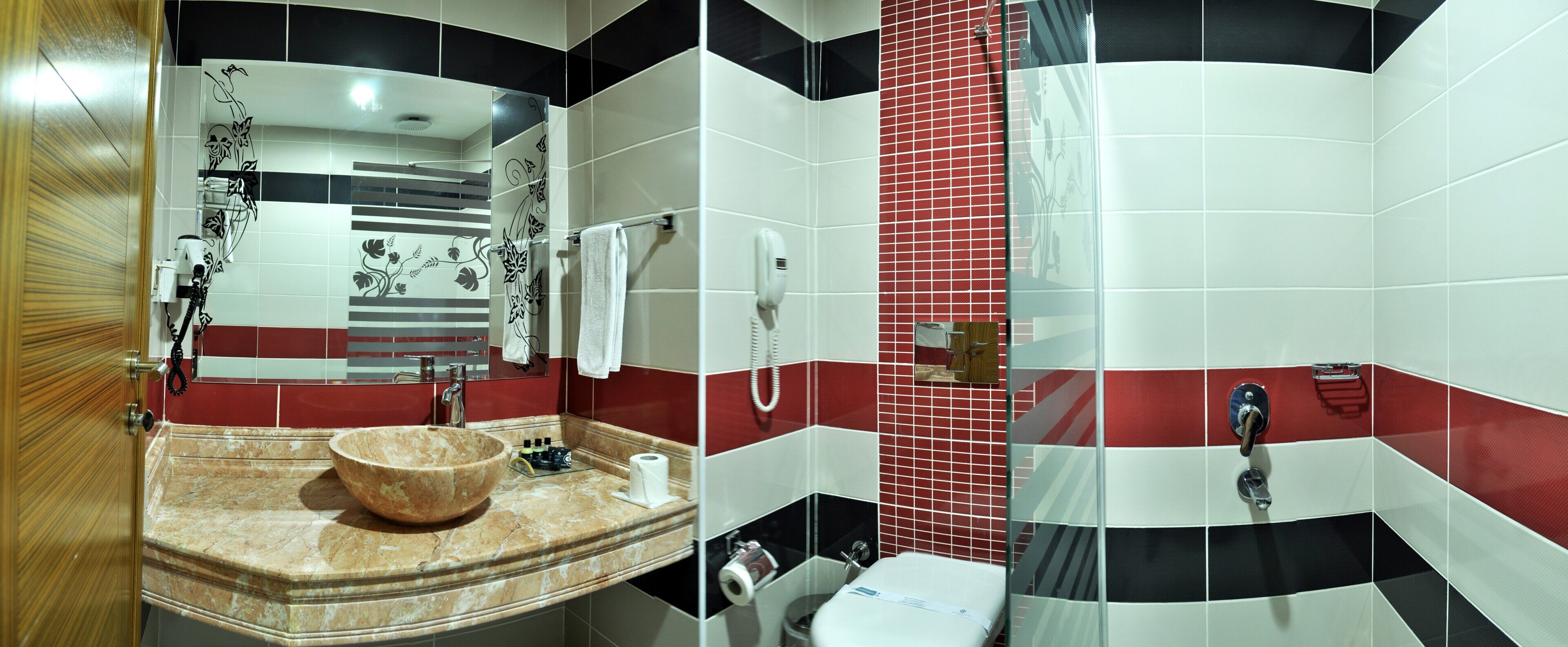 Une salle de bain dotée d’un grand lavabo en marbre, d’une cabine de douche en verre et de murs recouverts de carreaux rouges et blancs.