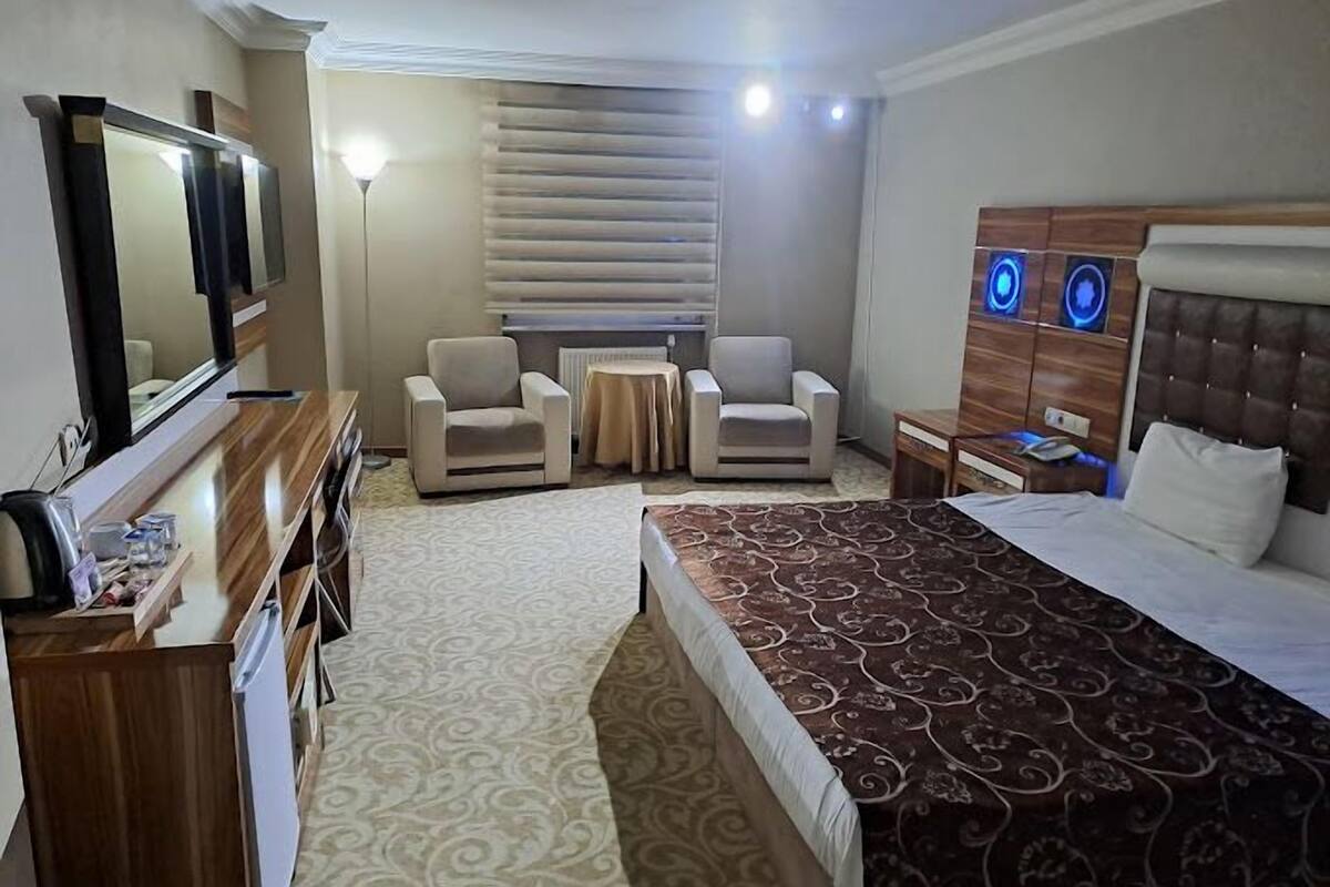 A hotel room with a bed, two armchairs, a small table, a TV, and a minibar.