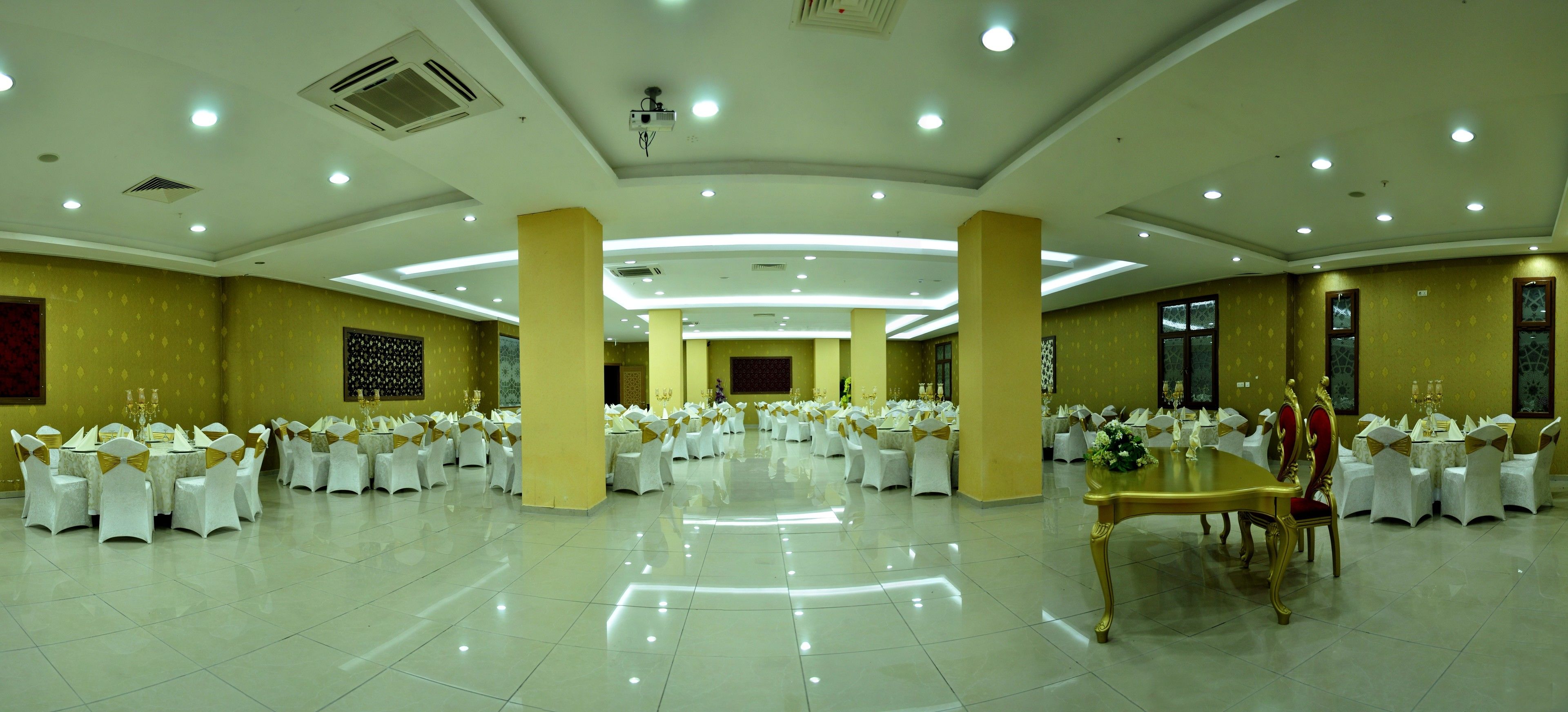 Un amplio salón de banquetes con varias mesas redondas y sillas, equipado con luces en el techo y unidades de aire acondicionado.