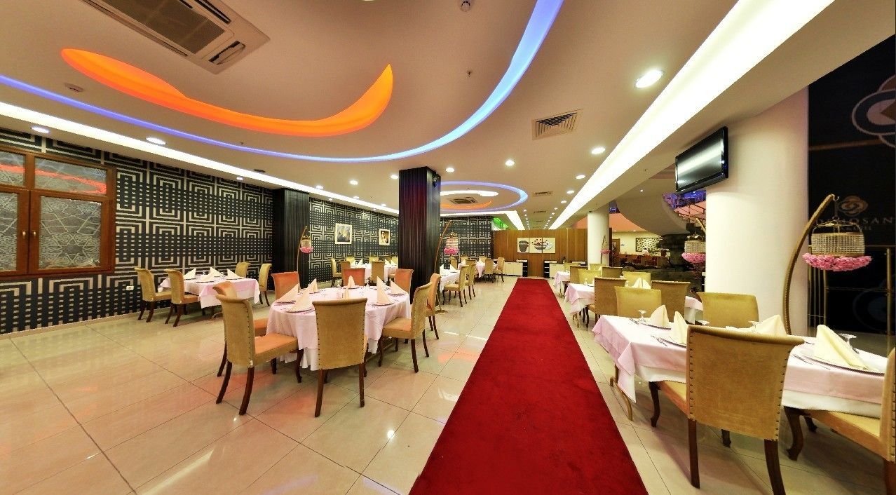 A hotel dining area with round tables, chairs, a red carpet, and a patterned wall.